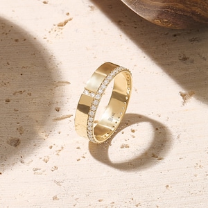 May include: A gold ring with a band of small, clear gemstones. The ring has a flat, rectangular design with a cross-like pattern of gemstones. The ring is marked with "14K".