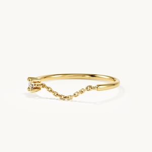 May include: A gold ring featuring a thin, polished band that transitions into a delicate, dangling chain section. One end of the chain is attached to a small, prong-set clear gemstone, while the other end connects to the solid portion of the ring band.