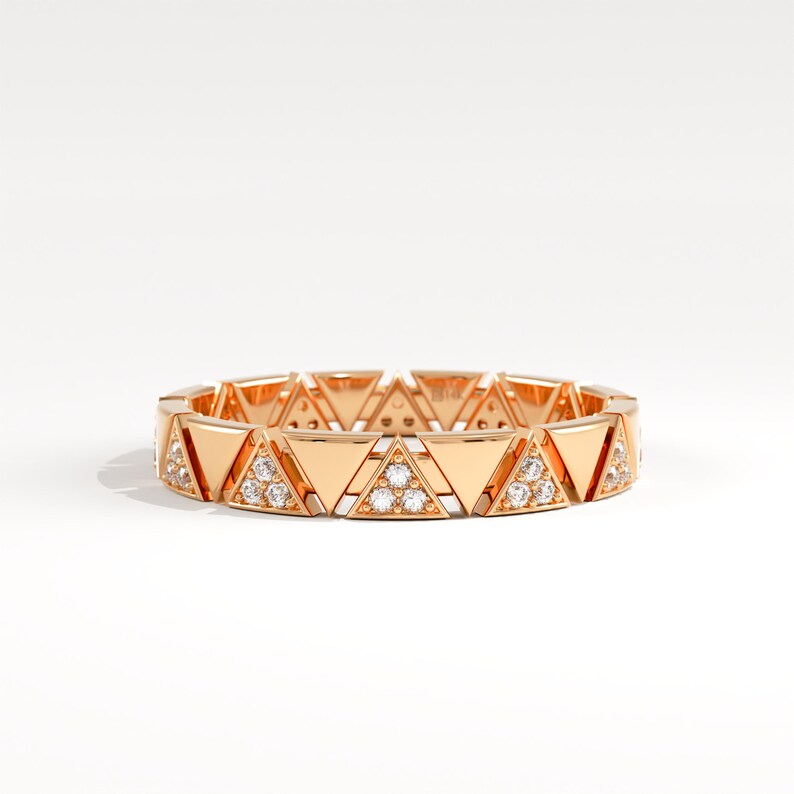 May include: A rose gold ring with a repeating triangular pattern. Each triangle is embellished with small diamonds. The ring's design is set against a white backdrop, emphasising its intricate details and elegant design. The ring's diameter is approximately 2 cm.