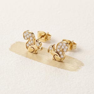 May include: A pair of gold stud earrings shaped like squirrels, each featuring a polished gold body and a tail encrusted with small, clear, round-cut white stones. The earrings have standard post backs and are designed for pierced ears.