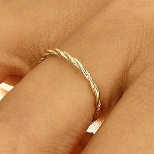 May include: A gold ring featuring a twisted rope design. The ring is worn on a finger, displaying its delicate and intricate pattern. The ring's shiny surface reflects light, highlighting its elegant and simple style.
