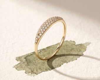 May include: A gold ring featuring a curved, tapered top section pavé-set with multiple small, clear, round-cut stones. The band is smooth and polished, with a visible 14K hallmark stamped on the inner surface of the metal shank.
