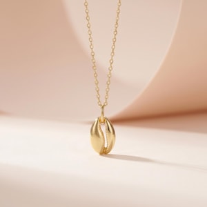 May include: A gold necklace with a seashell pendant. The pendant hangs from a fine chain. The background is a soft, neutral colour, which accentuates the jewellery.
