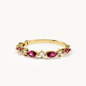 May include: A gold ring featuring a series of alternating marquise-cut pink gemstones and round-cut clear stones set along the band. The interior of the band is clearly stamped with the text 14K, indicating the metal purity of the jewelry piece.
