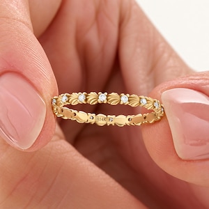 Könnte beinhalten: Ein Ring aus Gelbgold mit einem sich wiederholenden blattartigen Muster, das mit kleinen runden, klaren Steinen besetzt ist. Auf der Innenseite des Rings ist deutlich der Text 14K eingraviert, der den Goldgehalt des Schmuckstücks angibt.