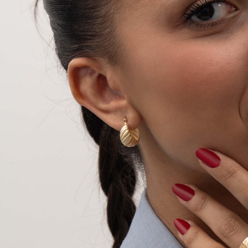 May include: A small gold hoop earring with a ribbed, textured surface. The earring features a rounded, semi-circular shape with vertical ridges that create a scalloped edge along the outer curve, secured with a simple hinged closure.