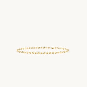 May include: A gold chain necklace composed of a series of small, circular, reflective discs linked together. Each disc features a textured, sunburst-like pattern that catches the light, creating a continuous, shimmering effect along the entire length.