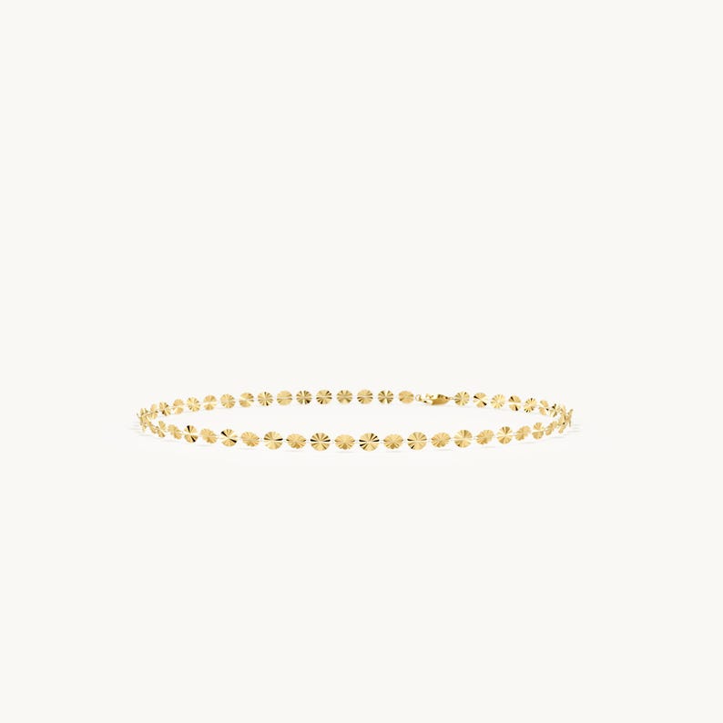 May include: A gold chain necklace composed of a series of small, circular, reflective discs linked together. Each disc features a textured, sunburst-like pattern that catches the light, creating a continuous, shimmering effect along the entire length.