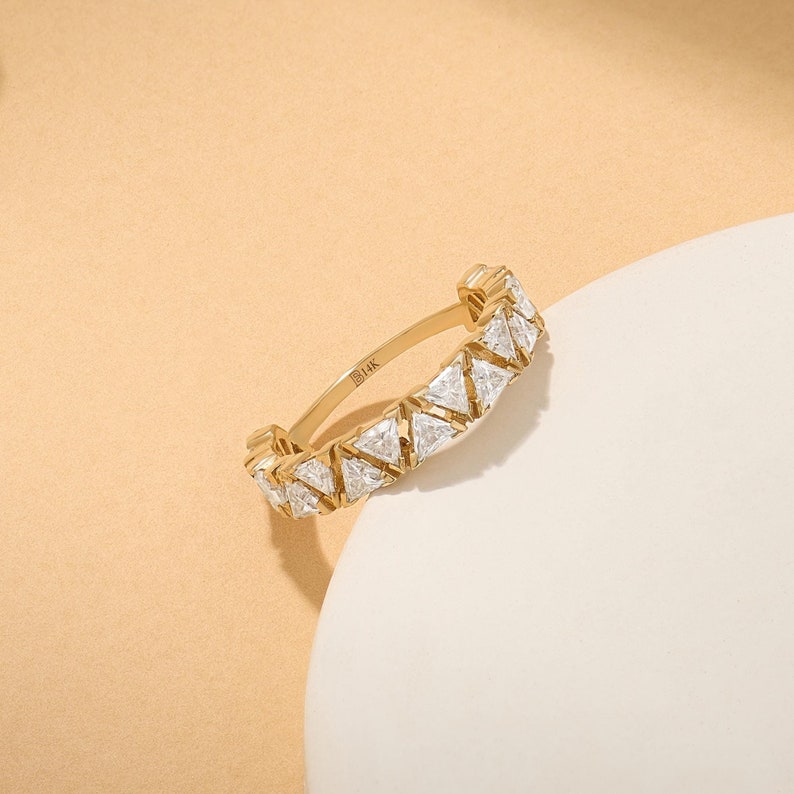 May include: A gold band ring with a row of triangular-shaped diamonds. The ring is marked "14K" on the inside.