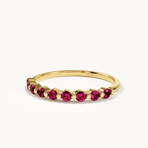 May include: A gold ring featuring a series of round, vibrant pink gemstones set in a row along the band. The metal band is polished yellow gold and includes a small 14K stamp on the inner surface, indicating the gold purity of the jewellery piece.