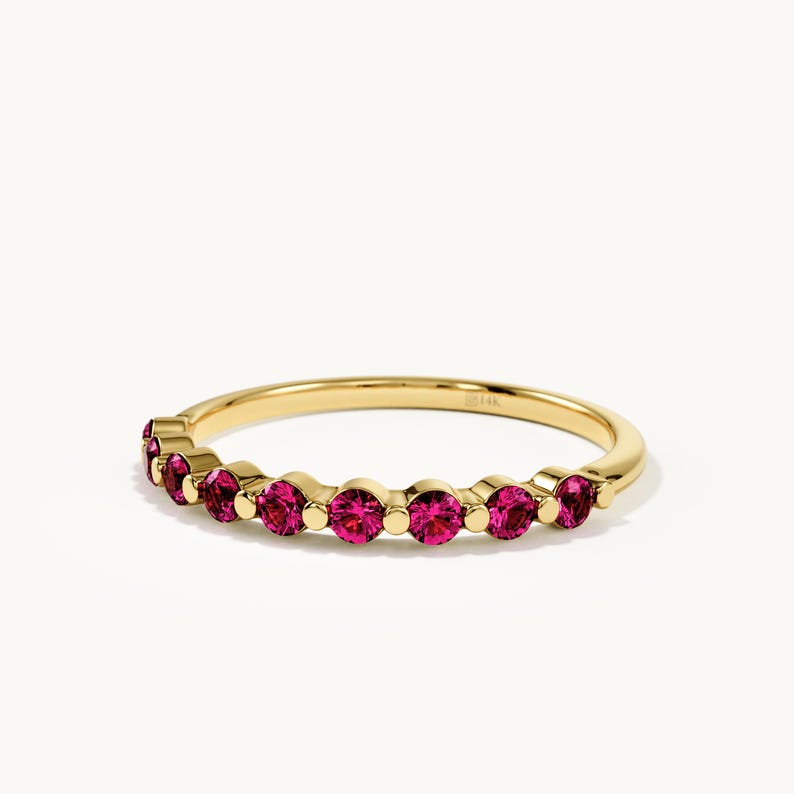 May include: A gold ring featuring a series of round, vibrant pink gemstones set in a row along the band. The metal band is polished yellow gold and includes a small 14K stamp on the inner surface, indicating the gold purity of the jewellery piece.