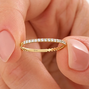 May include: A thin 14K gold band ring featuring a row of small, clear, round-cut stones set along the top half. The interior of the band is clearly stamped with the text 14K, indicating the gold purity of this delicate jewellery piece.
