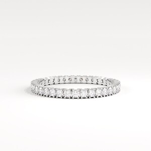May include: A silver eternity ring with a continuous row of round-cut, clear gemstones. The ring is set against a white background, showcasing the sparkle of the stones. A classic piece of jewelry.