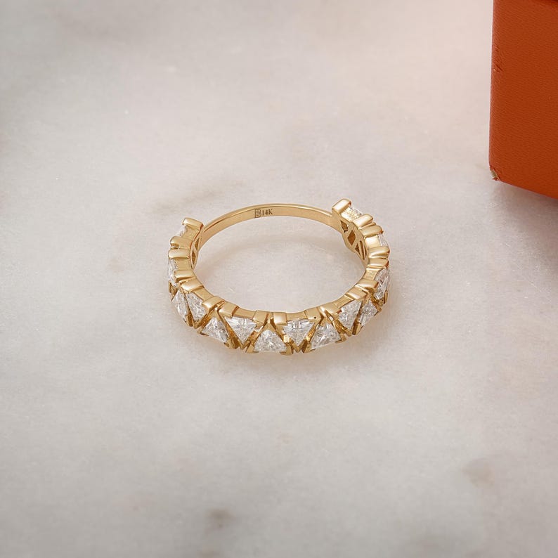 May include: A gold band ring with a row of triangular-shaped diamonds set in the band. The ring is marked "14k" on the inside.