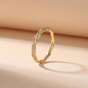 Op de afbeelding: Een 14K gouden ring met een gedraaid bandontwerp, ingelegd met kleine, heldere, rondgeslepen stenen op het oppervlak. De binnenkant van de ring is duidelijk gestempeld met de tekst 14K.