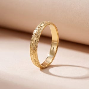 May include: A gold ring with an engraved leaf pattern. The ring is a warm gold color and has a smooth, polished finish. The inside of the ring is stamped with "B14K". The ring is a classic design, suitable for everyday wear or special occasions.