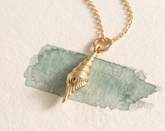 May include: A gold-toned necklace featuring a pendant shaped like a spiral seashell. The pendant is suspended from a delicate gold-toned chain, showcasing a detailed, textured surface that mimics the natural ridges of a shell.