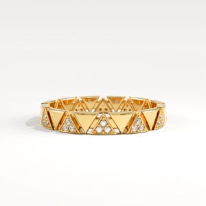 May include: A gold ring with a repeating triangular design. Each triangle is set with small gemstones. The ring has a polished finish and a contemporary, geometric style. The design is suitable for everyday wear or special occasions.