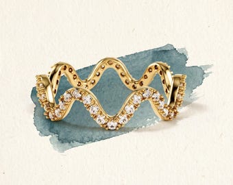 May include: A gold ring featuring a continuous wavy or serpentine band design. The surface of the gold band is encrusted with a series of small, clear, sparkling stones that follow the undulating shape of the metal throughout the entire ring.