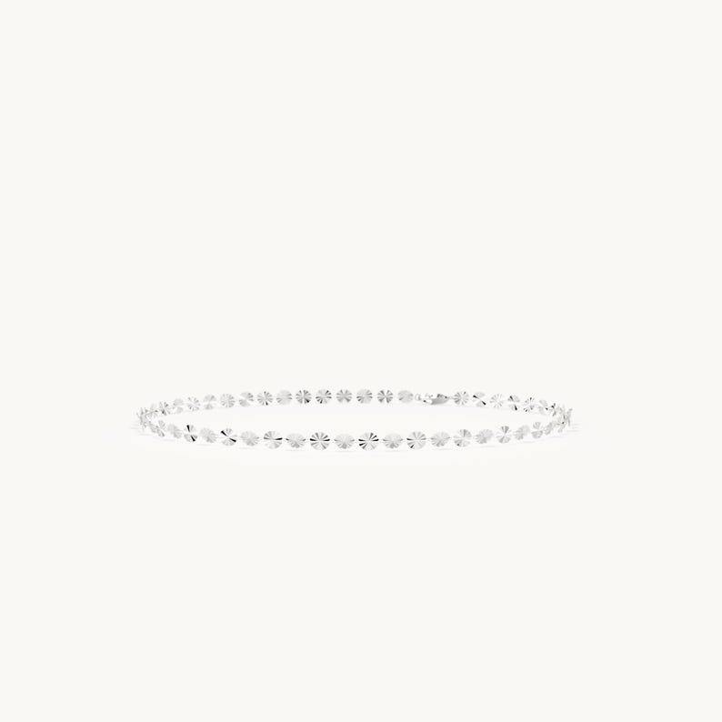 May include: A silver chain bracelet composed of a series of small, circular, faceted metallic discs linked together. The reflective surface of each individual disc catches the light, creating a shimmering effect along the entire length of the bracelet.
