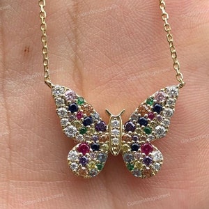 Può includere: Una collana con catena d'oro con un ciondolo a forma di farfalla. La farfalla è decorata con pietre preziose colorate, tra cui rosso, blu, verde, giallo e viola.