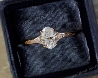 May include: A rose gold engagement ring with an oval-shaped center stone and two smaller accent stones on each side. The ring is in a blue velvet ring box.