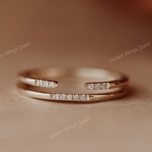 May include: A delicate gold ring with two bands, one with a row of small diamonds. The ring is on a brown surface.