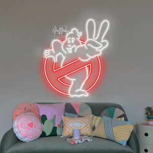 May include: A white neon sign of a ghost with a red circle and a diagonal line through it. The sign is on a wall above a green velvet sofa with colorful throw pillows.