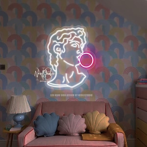 Peut inclure: Un canapé rose avec trois coussins et une couverture se trouve devant un mur à motif arc-en-ciel. Un néon représentant un homme soufflant une bulle est sur le mur. Le texte sur le néon indique "LED Neon Sign Design by Neollstudio".