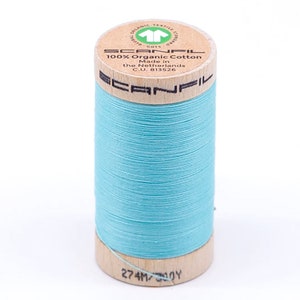 May include: A spool of light blue 100% organic cotton thread from Scanfil, made in the Netherlands. The spool is labeled with the brand name, thread type, and length: 274 meters / 300 yards.