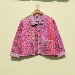 Pode incluir: Uma jaqueta acolchoada rosa com estampa floral e fecho de botões. A jaqueta tem dois bolsos de remendo na frente e uma gola listrada.