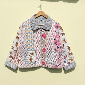 May include: A quilted jacket with a patchwork design featuring floral, tiger, and geometric patterns. The jacket has a striped collar and cuffs, with two front pockets. The color palette includes white, pink, blue, and brown.