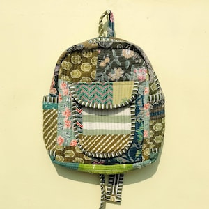 Puede incluir: Una mochila de estilo patchwork con un esquema de color verde, azul y marrón. La mochila tiene un cierre de cordón y un pequeño bolsillo en la parte delantera.