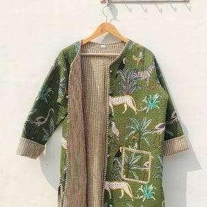 Pode incluir: Uma jaqueta acolchoada verde com forro listrado. A jaqueta apresenta um padrão de animais e plantas, incluindo um leopardo, uma zebra, um tucano e palmeiras.