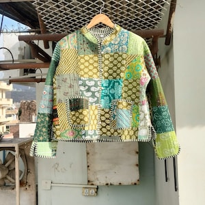 Può includere: Una giacca trapuntata patchwork verde e gialla con colletto alla coreana e maniche lunghe. La giacca è realizzata con una varietà di tessuti e ha un aspetto unico e fatto a mano.