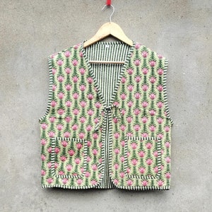 Pode incluir: Um colete de estampa floral verde e rosa com forro listrado e fecho de gravata. O colete tem dois bolsos na frente.