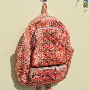May include: A patchwork quilted backpack with a floral print in shades of orange and pink. The backpack has a zippered pocket on the front and a top handle.