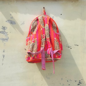 Puede incluir: Una mochila rosa y naranja con un diseño de estampado de tigre. La mochila tiene un cierre de cordón y una solapa con una hebilla.