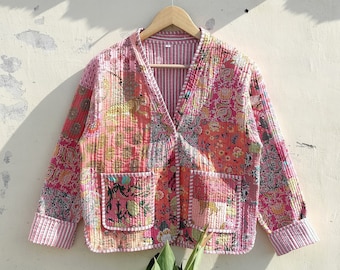 May include: A pink quilted jacket with a patchwork design featuring floral and geometric patterns. The jacket has a V-neck, long sleeves, and a button closure.