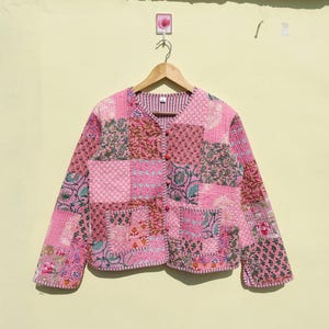 Puede incluir: Una chaqueta acolchada rosa con un diseño de patchwork que presenta varios patrones florales. La chaqueta tiene un cierre de botón y mangas largas.
