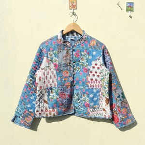 Puede incluir: Una chaqueta acolchada azul con estampado floral. La chaqueta tiene un cuello mandarín y cierre de botón. Las mangas son largas y la chaqueta está forrada con un tejido blanco.