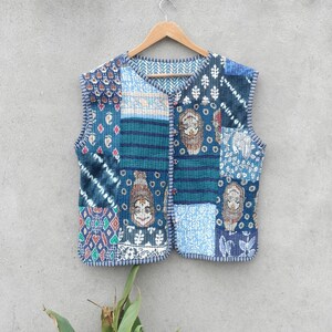 May include: A blue quilted vest with a patchwork design featuring various patterns and colors. The vest has a button closure and a sleeveless design.