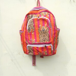 Op de afbeelding: Gewatteerde rugzak met een tijgerstreepmotief in oranje, roze en wit. De rugzak heeft een voorvak, zijvakken en een handvat aan de bovenkant. Het ontwerp bevat een herhaald tijgermotief.