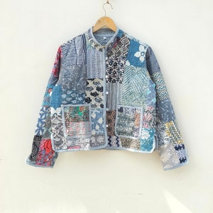 May include: A blue quilted jacket with a patchwork design featuring various floral and geometric patterns. The jacket has a mandarin collar, a button closure, and two patch pockets.