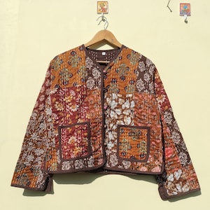 Könnte beinhalten: Eine braune gesteppte Jacke mit Blumendruck und zwei Taschen. Die Jacke hat einen Knopfverschluss und einen Stehkragen.