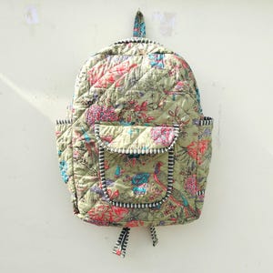 Può includere: Zaino trapuntato verde oliva con motivo floreale e di uccelli. Presenta una tasca frontale e tasche laterali, tutte rifinite con tessuto a righe bianche e nere. Include un manico superiore e spallacci regolabili.