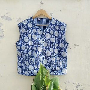 Può includere: Un gilet trapuntato blu e bianco con un motivo floreale. Il gilet ha una chiusura con bottone ed è senza maniche.