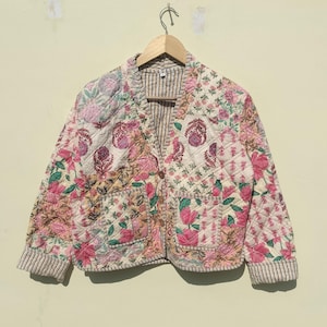 May include: A cream-colored quilted jacket with a floral patchwork design. The jacket has a button closure and two pockets. The sleeves have a striped pattern.