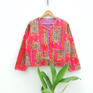 Pode incluir: Uma jaqueta acolchoada rosa e laranja com estampa de tigre. A jaqueta tem fecho de botão e dois bolsos de remendo.