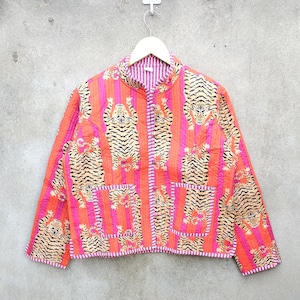 Può includere: Giacca trapuntata con stampa di tigre. La giacca presenta un motivo ripetuto di tigri su uno sfondo di strisce verticali nei toni del rosa e dell'arancione. Ha due tasche anteriori e una chiusura con bottoni.